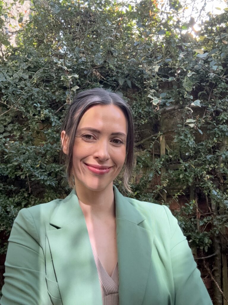 Women wearing green jacket, standing against green trellis background